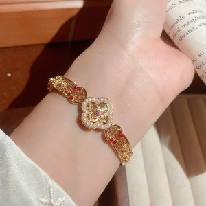 Close-up of vintage gold bangle with hollow clover patterns, pearls and red gemstones