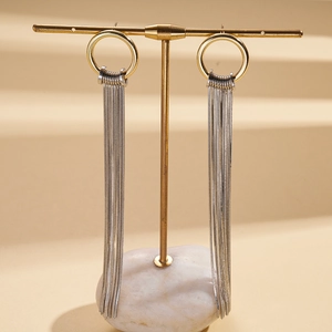 Detail of 18K gold plated round earrings with long silver tassels on a marble stand