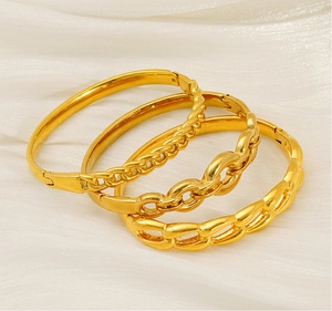 Detailed view of three gold-plated stainless steel bangles on white silk background