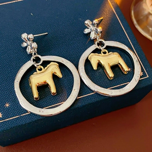 Detailed view of silver flower studs with gold horse charm pendants on jewelry box