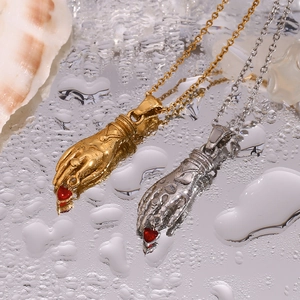 Detail of gold and silver hand-holding red heart necklaces on a wet mirror background