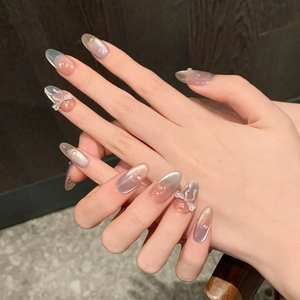 Detail of long oval press-on nails with 3D white bows, pearls, and cat eye gradient finish