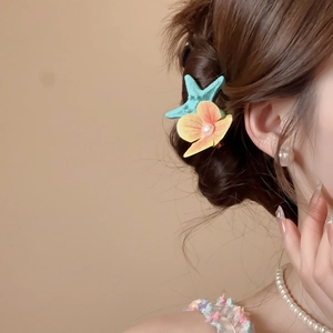 Detail of mint starfish and yellow floral hair clip with pearl on woman's hair