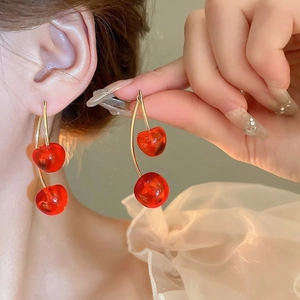 Close-up of model wearing vibrant red cherry earrings with gold-toned metal stems