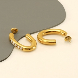 Detail of gold C-shaped earrings with five white pearls on a minimalist background