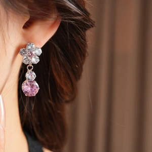 Detailed close-up of a flower-shaped zircon earring with pink stones on a female model