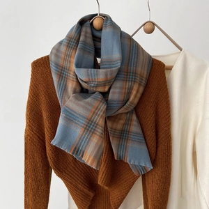 Detail of grey-blue and orange checkered scarf with fringe on a wooden hanger