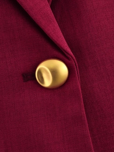 Detailed macro view of a gold textured metal button on burgundy twill blazer fabric
