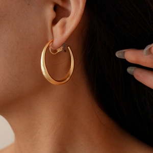 Close-up of a minimalist golden C-shaped geometric metal ear clip on a model ear