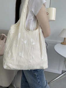 Detail of white floral embroidery on a soft textured cream canvas tote bag for women