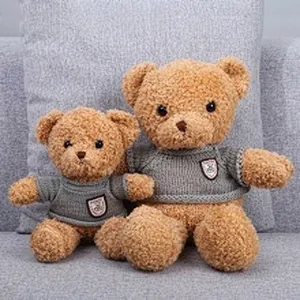Detail of two plush teddy bears in grey sweaters sitting on a sofa, large and small size