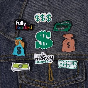 Set of nine money-themed enamel pins displayed on a blue denim jacket pocket