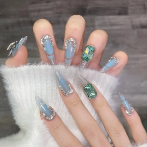 Detail of luxury stiletto press-on nails with blue gradient, emerald gems and pearls