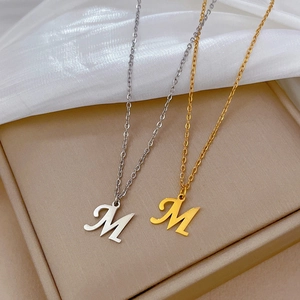 Minimalist gold and silver M letter pendant necklaces on elegant white silk background