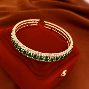 Detailed shot of double-row gold bangle with emerald green gems and clear zircon stones
