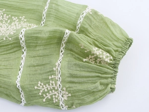 Detail of green dress sleeve with floral embroidery and white lace stitching