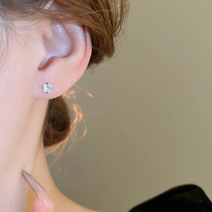 Close-up of a sparkling zircon stud earring on ear with minimalist silver setting