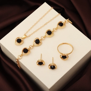 Detail of four-piece gold jewelry set with black crystal heart pendants on silk fabric