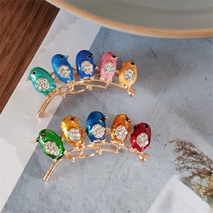 Detail of two colorful enamel bird brooches on golden branches with sparkling rhinestones