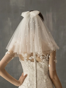 Detail of white bridal veil with delicate pearls and bow knot on multilayered tulle