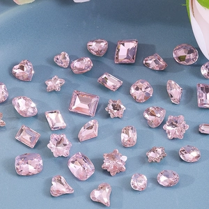 Flat lay of pink faceted nail art rhinestones in various shapes like heart and star