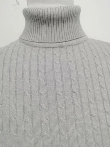 Dettaglio del maglione grigio a collo alto con trama a trecce intrecciata e consistenza