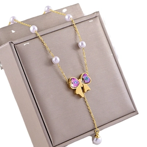 Collier papillon doré avec cristaux de cœur violets et perles blanches sur boîte à bijoux