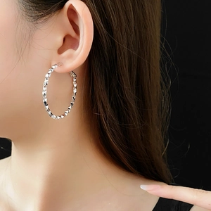 Dettaglio di un grande orecchino a cerchio argento con texture sfaccettata su modella