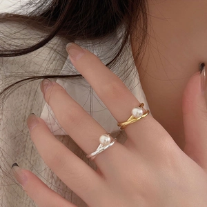 Detailed view of silver and gold crisscross pearl rings on finger with polished finish