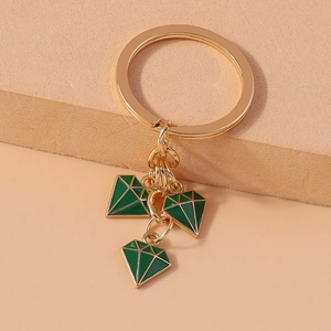 Detail of golden keychain with three green enamel diamond-shaped pendants on textured surface