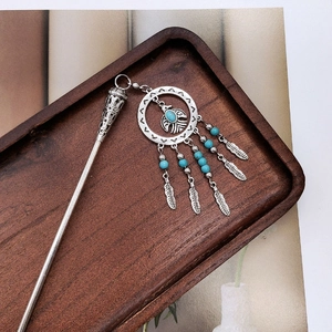 Detailed close-up of ethnic silver hair stick with eagle feather charms and turquoise beads