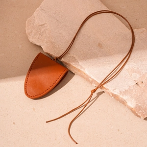 Detail view of orange-brown faux leather magnetic triangle pendant on beige stone