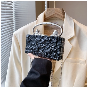 Detail of black pleated acrylic evening bag with silver lion-shaped metal handle and chain