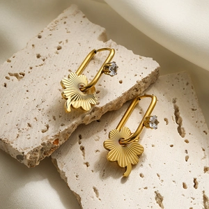 Minimalist gold four-leaf clover drop earrings with clear gemstones on stone background