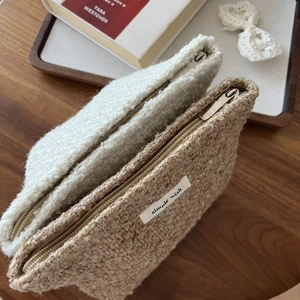 Close-up of cozy beige and tan tweed makeup bags with metal zippers on a wooden table