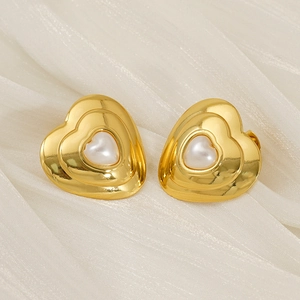 Detail of golden heart-shaped earrings with central pearl on soft beige silk fabric