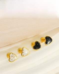 Détail de boucles d'oreilles cœur avec émail noir et blanc et accents pailletés dorés