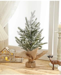 Close-up of mini snow-flocked Christmas tree with rustic burlap base on a festive windowsill