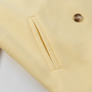 Detail of pale yellow wool coat showing double-breasted buttons and fabric texture