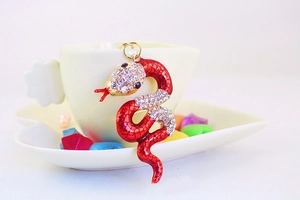 Detailed view of red enamel snake keychain with sparkling rhinestones on a coffee cup