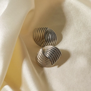 Macro shot of silver textured knot earrings resting on elegant beige silk fabric