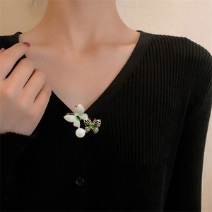 Detail view of double butterfly brooch with green gems and a hanging pearl on a collar
