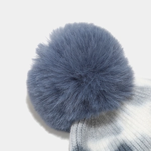 Dettaglio del pompon blu in ecopelliccia su un cappello in maglia tie-dye grigio e bianco