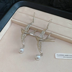Makro-Detail von Schwalben-Perlenohrringen aus Silber auf einem beigen Samt-Tablett