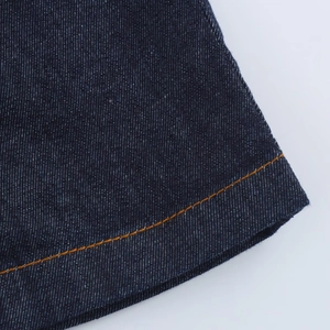 Detail van contrastrerende oranje stiksels op de diepblauwe denim zoom van jurk