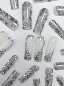 Macro detail of long square press-on nails with marble pattern and silver heart rhinestones