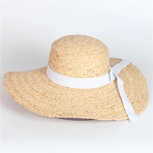 Detailed close-up of natural raffia weave and white ribbon bow on wide-brim sun hat