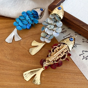 Macro detail of fish-shaped hair clips in blue, pearl white and red with evil eye accent