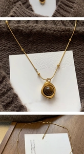 Macro detail of gold stainless steel necklace with round brown tiger eye stone pendant