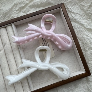 Detailed view of pink and white ink-wash style bow hair claws on a jewelry tray